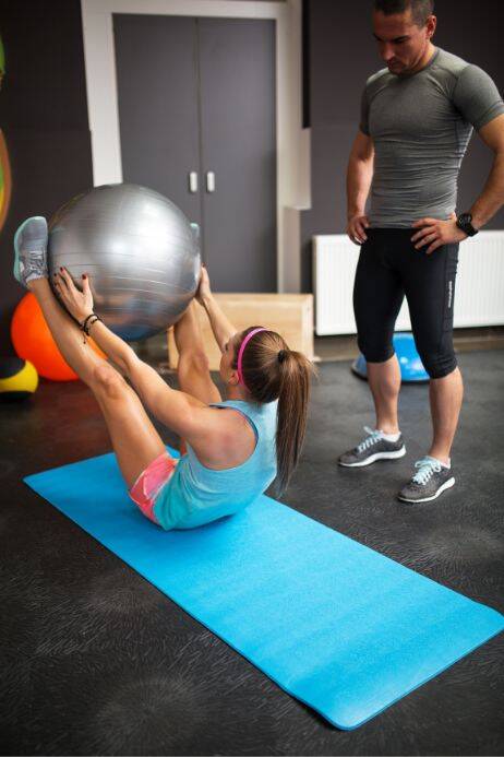 Fitness instructor supervising a client using an exercise ball, emphasizing need for liability insurance in gym settings.