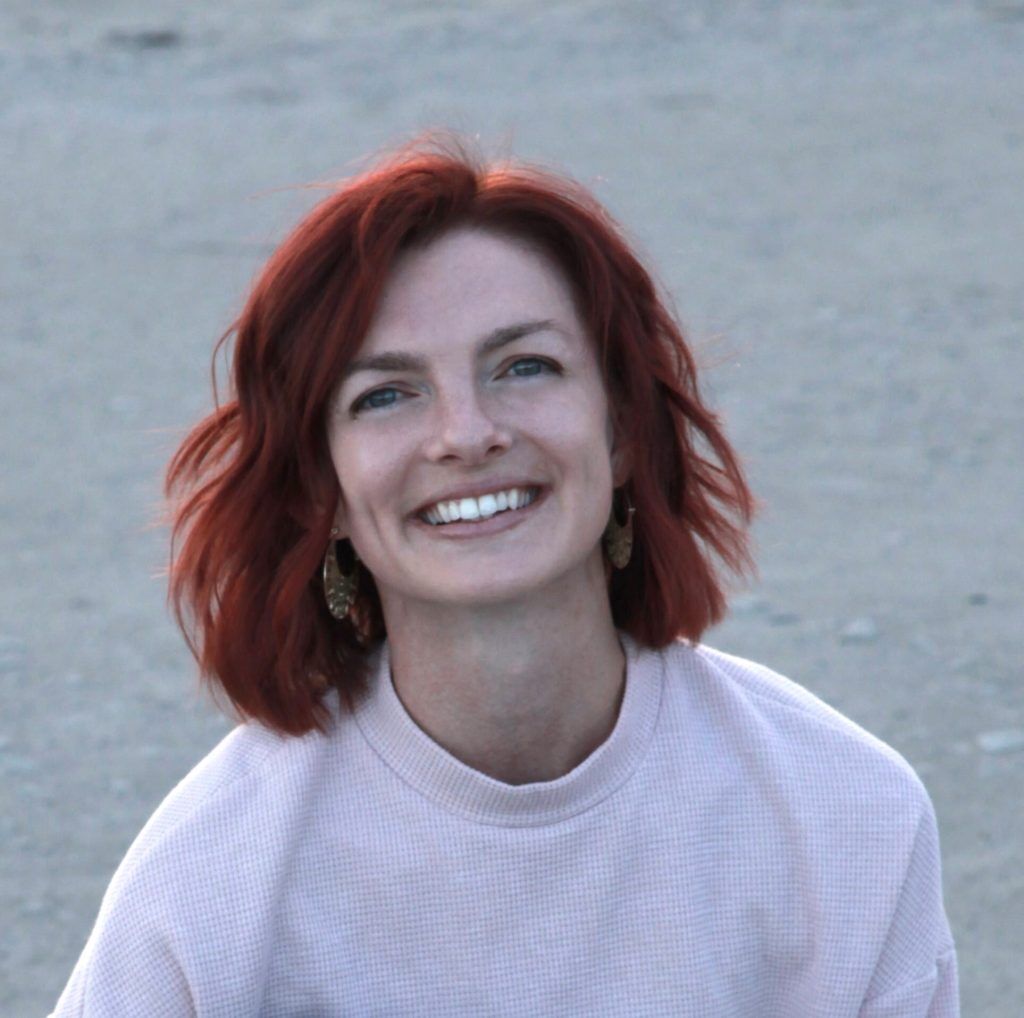 Woman with red hair and a pink sweatshirt smiling