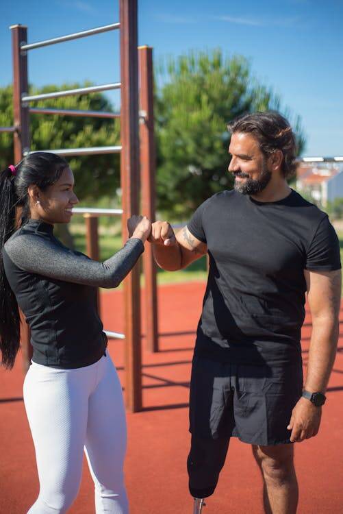 Free Two athletes celebrate a workout accomplishment with a fist bump in a park setting, highlighting teamwork and inspiration. 
