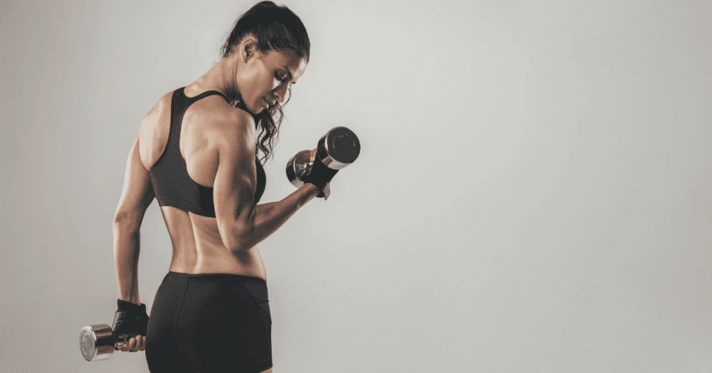 A strong woman lifting dumbbells, showcasing muscular definition and focus, symbolizing personal trainers' ability to specialize in different fitness areas.