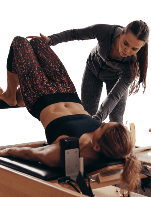 Pilates instructor guiding a client on a reformer machine, demonstrating proper form and technique in a studio setting.