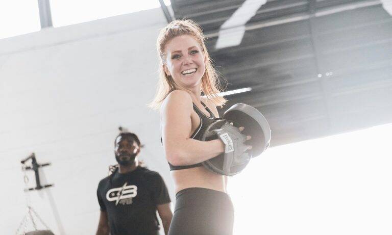 A woman in sparring gear smiles at the camera.